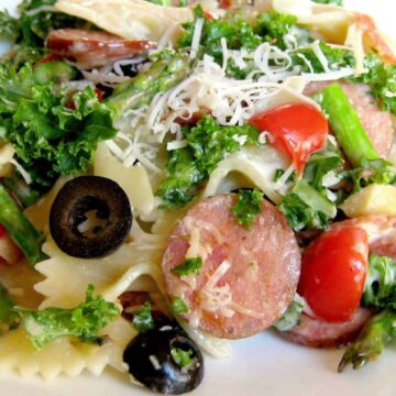 A plate of pasta salad with olives, kale and sausage