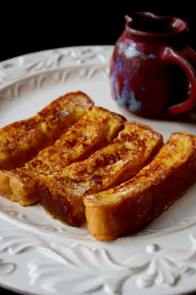 Eggnog French Toast Sticks on plate with cup of syrup