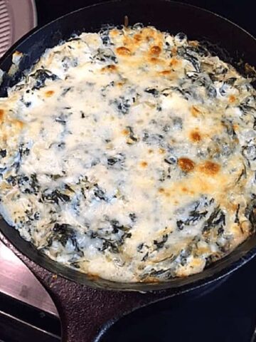 brown melted cheese on creamy spinach dip in black skillet