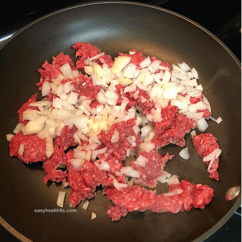 raw ground beef and chopped onions in skillet