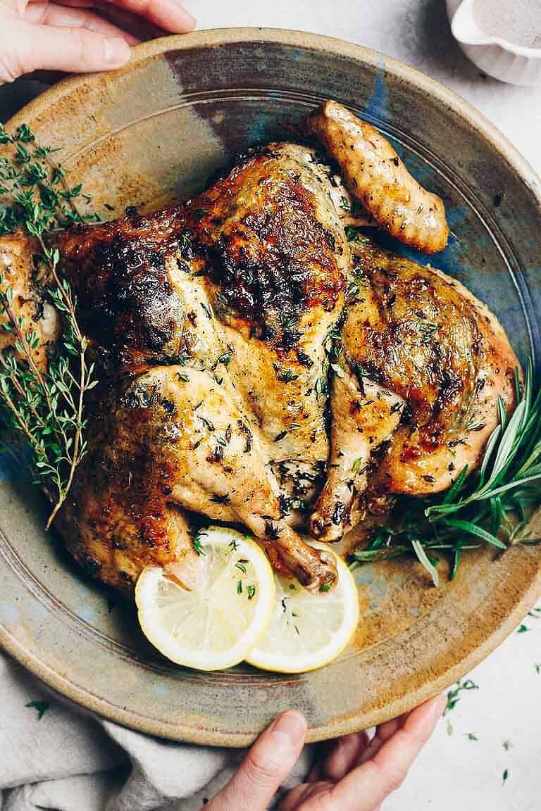 golden brown roasted chicken with sprinkled herbs on platter with sliced lemons and rosemary stems