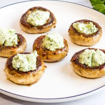 green goddess stuffed mushroom halves on white plate with garlic cloves and parsley to the side