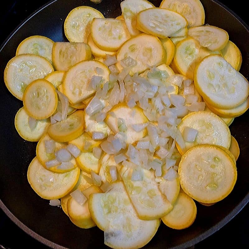 uncooked sliced yellow squash and diced onion in black skillet