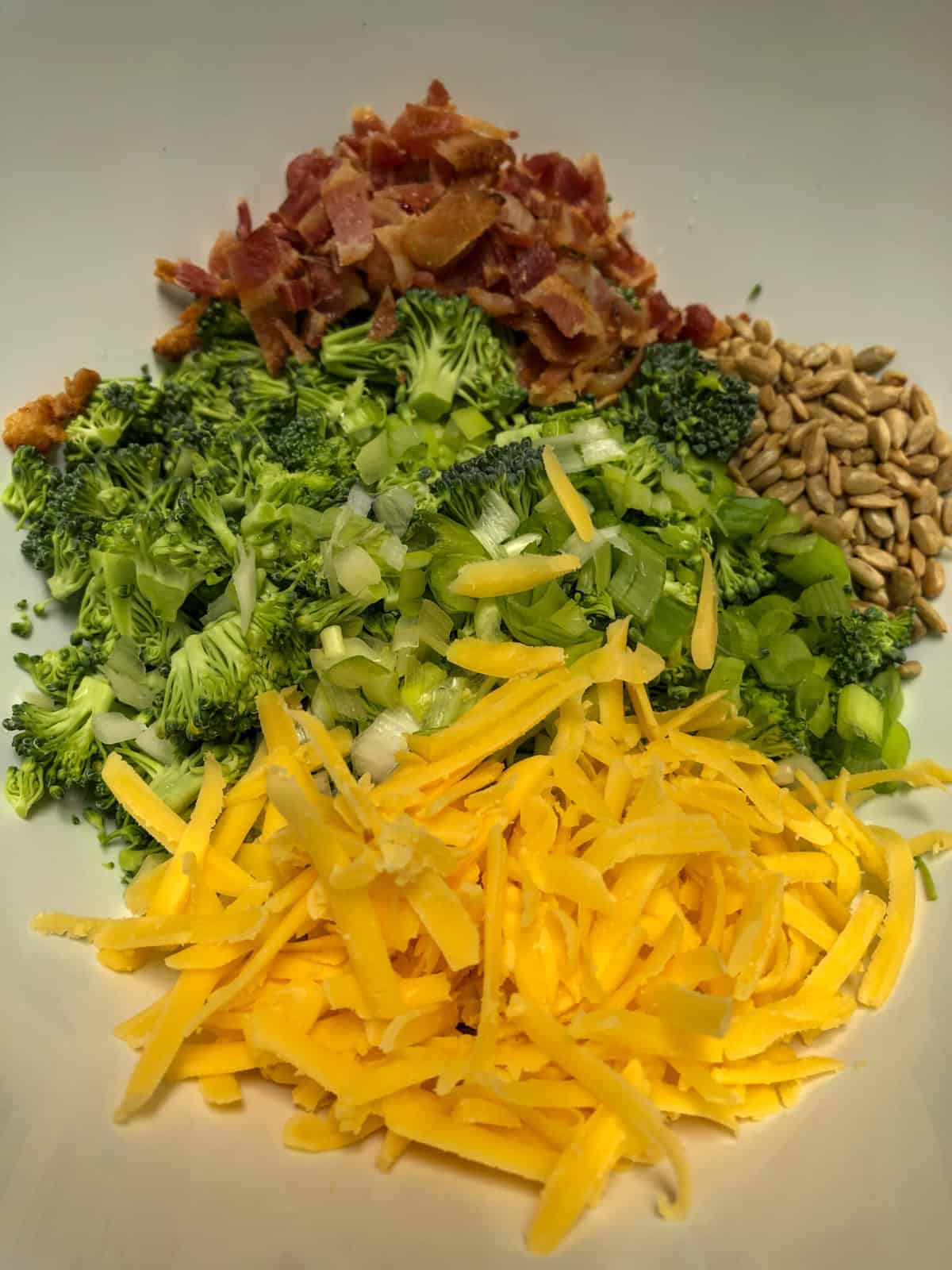 chopped broccoli, diced bacon, grated cheese, sunflower seeds in white bowl