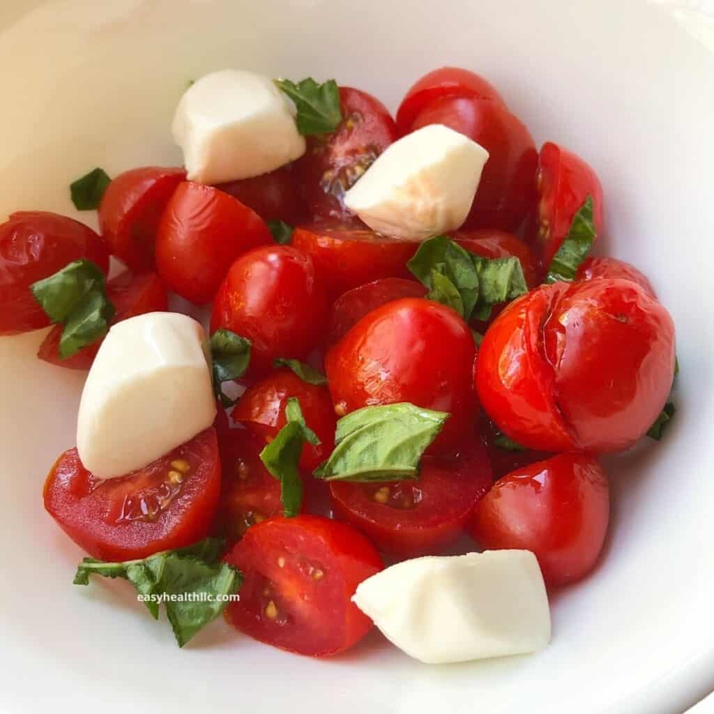 cherry tomatoes, mozzarella cheese chunks and torn basil leaves salad in white bowl