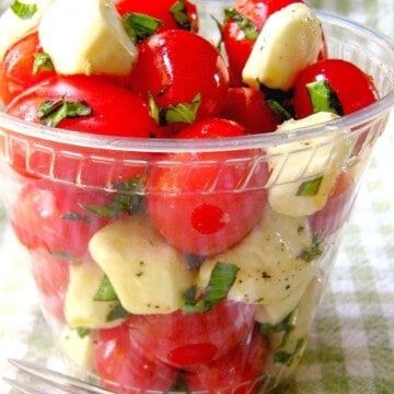 cherry tomatoes, mozzarella balls and torn basil leaves in a clear plastic cup