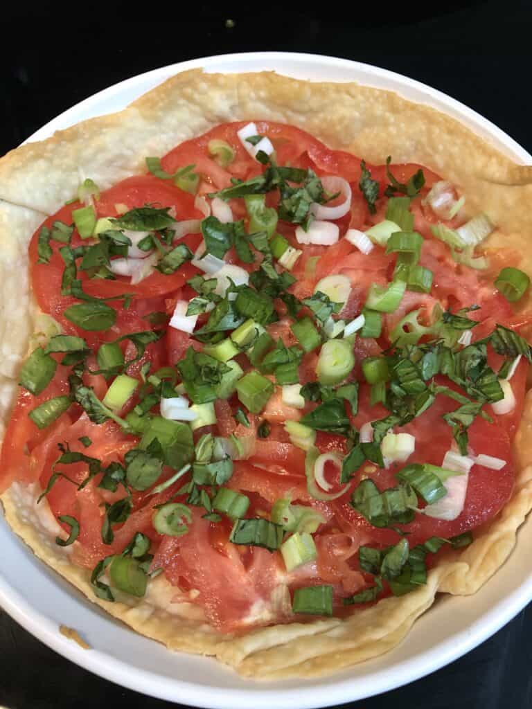 green onions and basil layered over tomato slices in baked crust