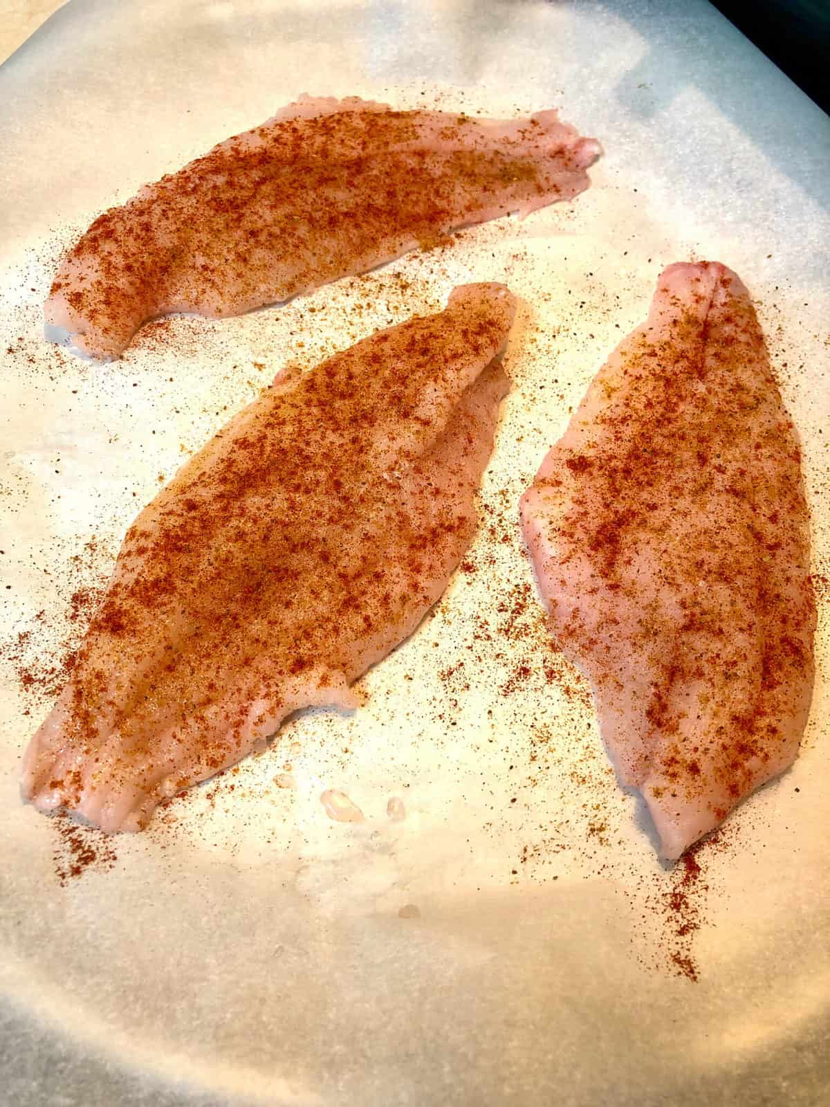 raw catfish with seasoning on baking sheet