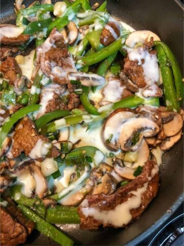 browned steak with green peppers and mushrooms and melted queso in black skillet