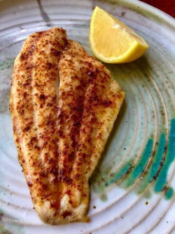 baked fish with lemon wedge on pottery plate