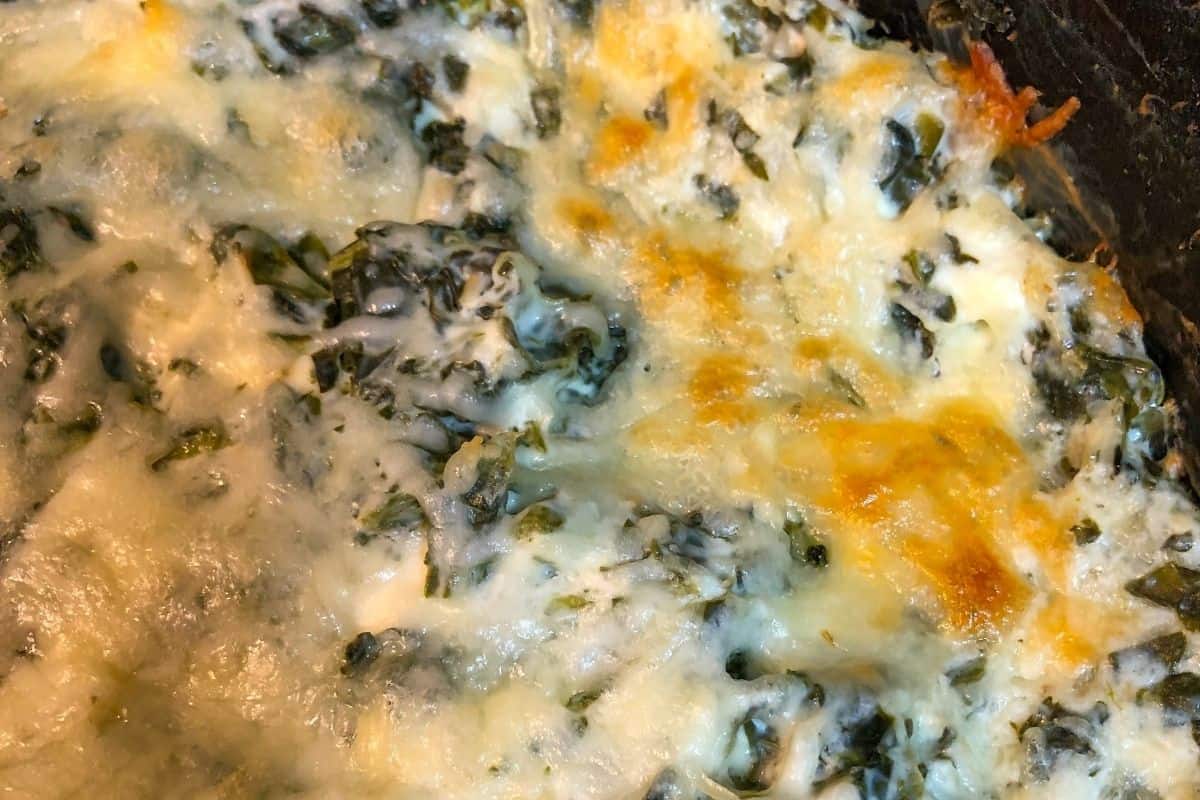 golden melted cheese and green spinach in black skillet