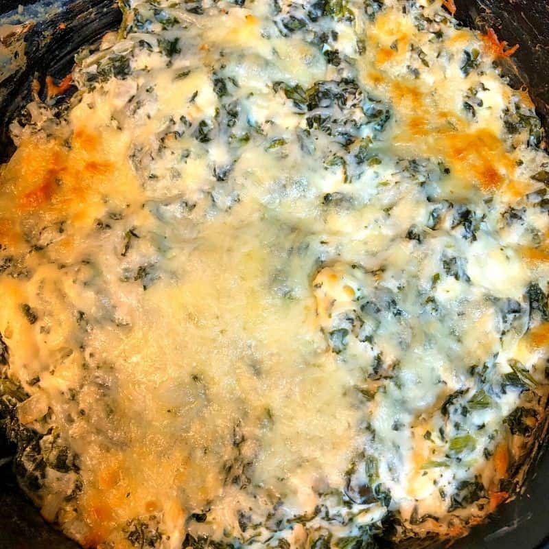 golden baked cheese over spinach dip in black skillet