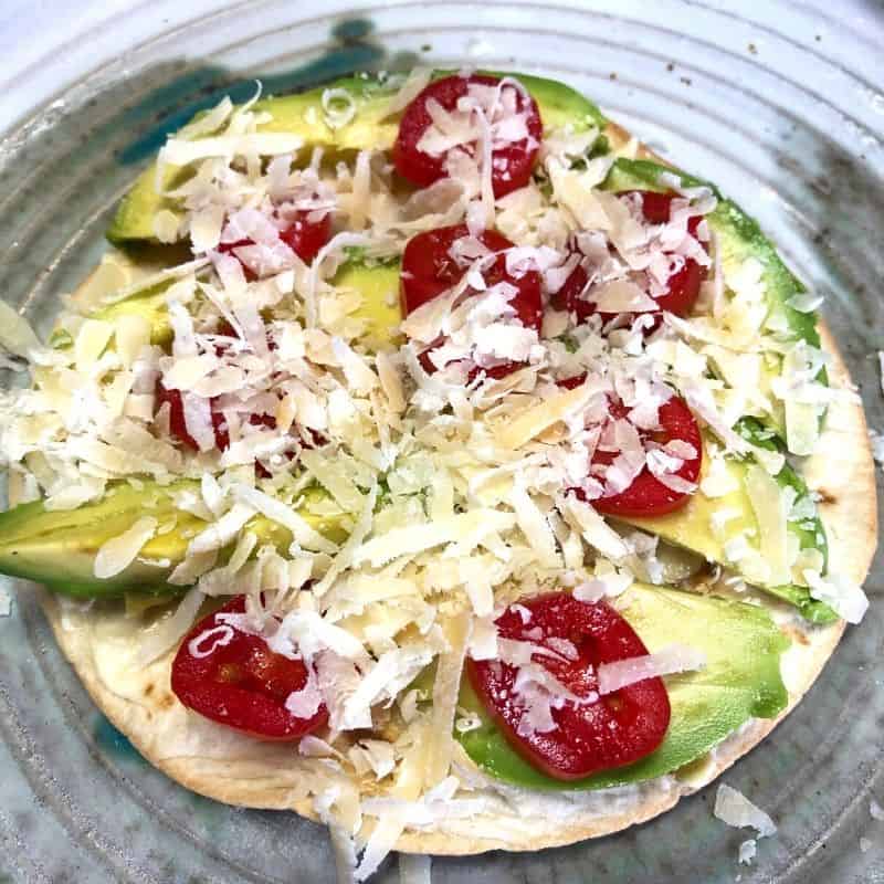 tortilla with avocado slices tomatoes and grated cheese ready for oven