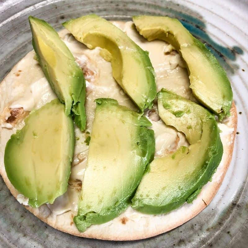 tortilla with cheese spread and sliced avocado