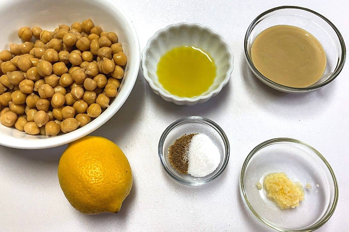 bowl of chickpeas, lemon,bowl of tahini, bowl of olive oil on white board