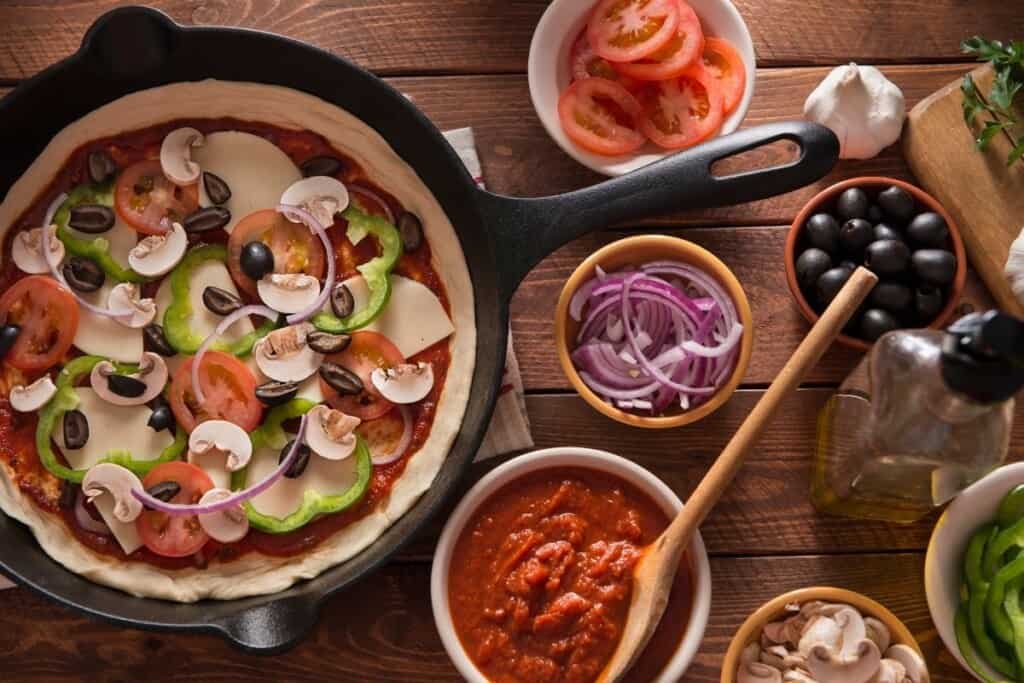 bowls of pizza sauce, red onion slices, sliced tomatoes with pizza in skillet