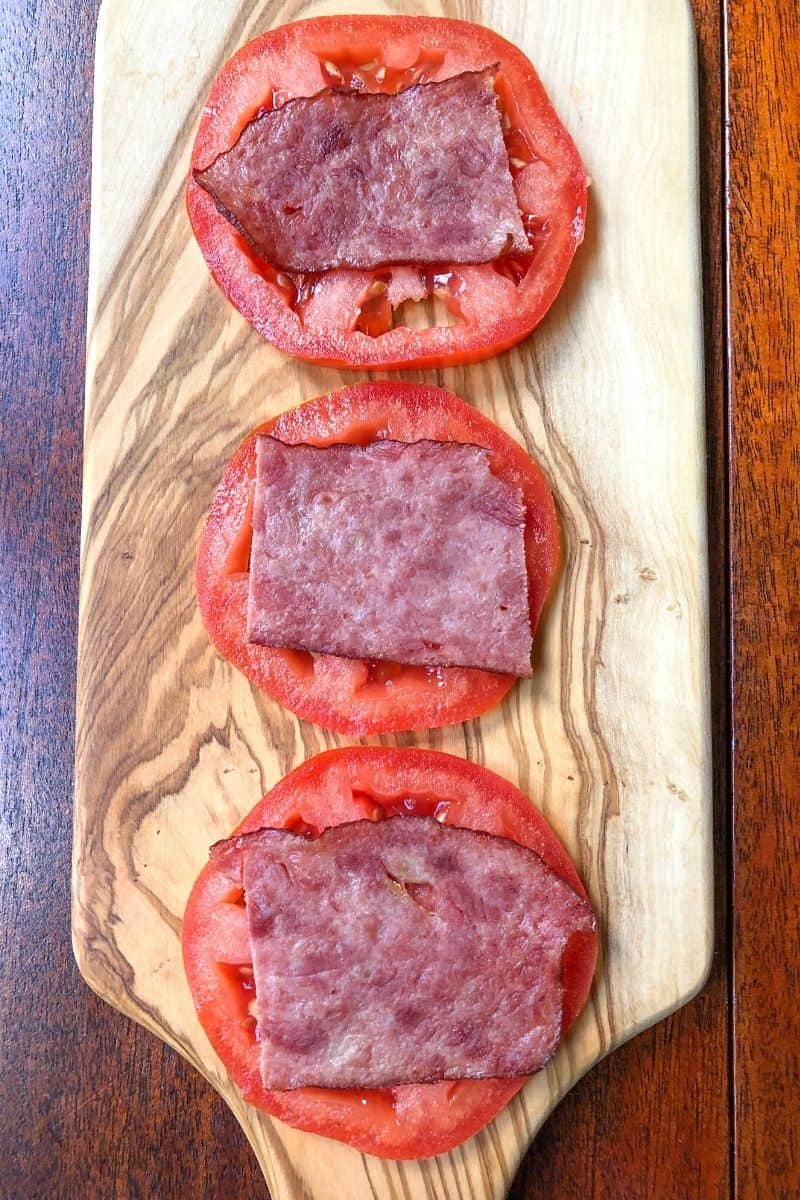 tomato slices topped with turkey bacon on wooden board