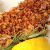 catfish fillet coated in chopped pecans with lemon wedge on white plate