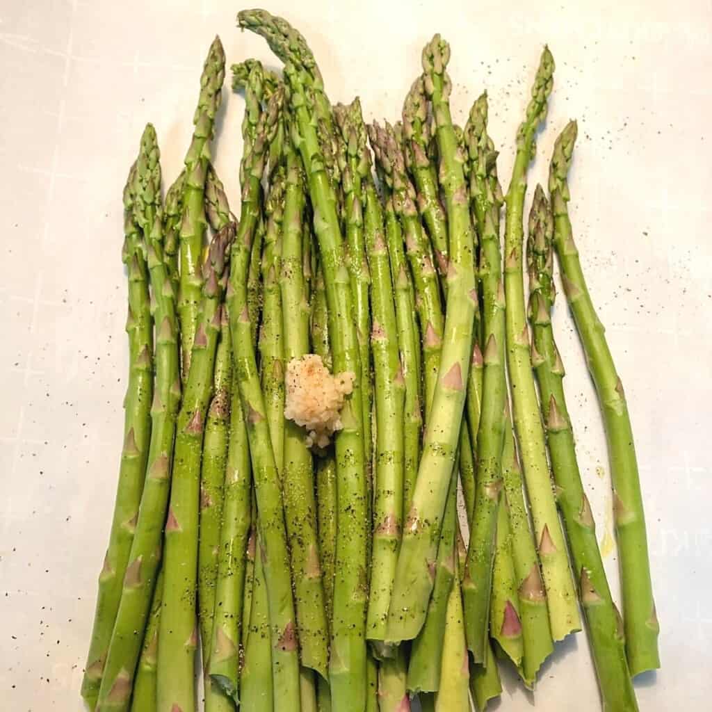 asparagus spears on white parchment paper with scoop of minced garlic on top