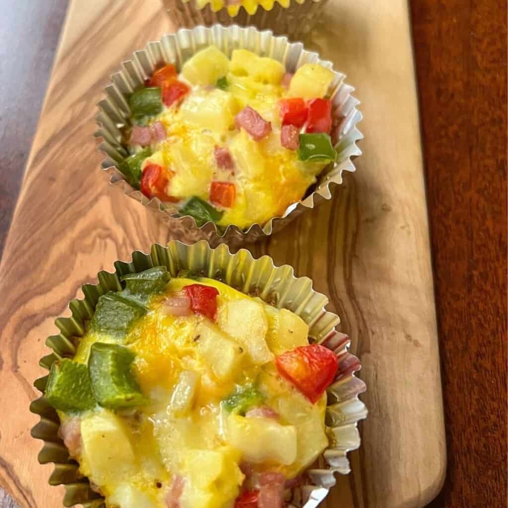 egg cups with diced potatoes and red and green peppers on wooden cutting board