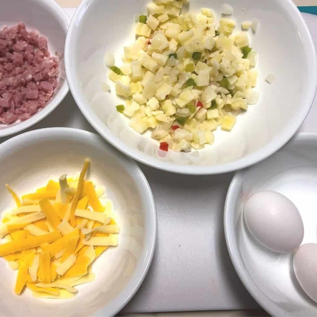bowls of eggs in shell, diced potatoes, grated cheese and diced ham