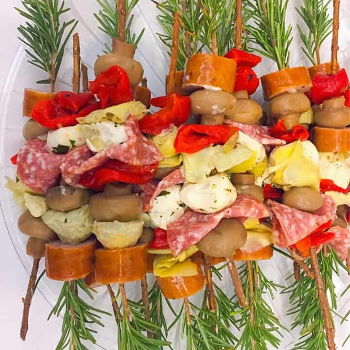rosemary skewers with sliced sausage, cheese and artichokes on white plate