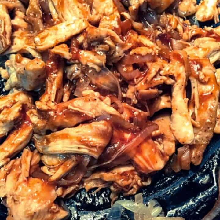 shredded chicken thighs with bbq sauce in iron skillet