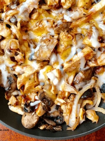 shredded chicken thighs with onions, bbq sauce and melted cheese in iron skillet