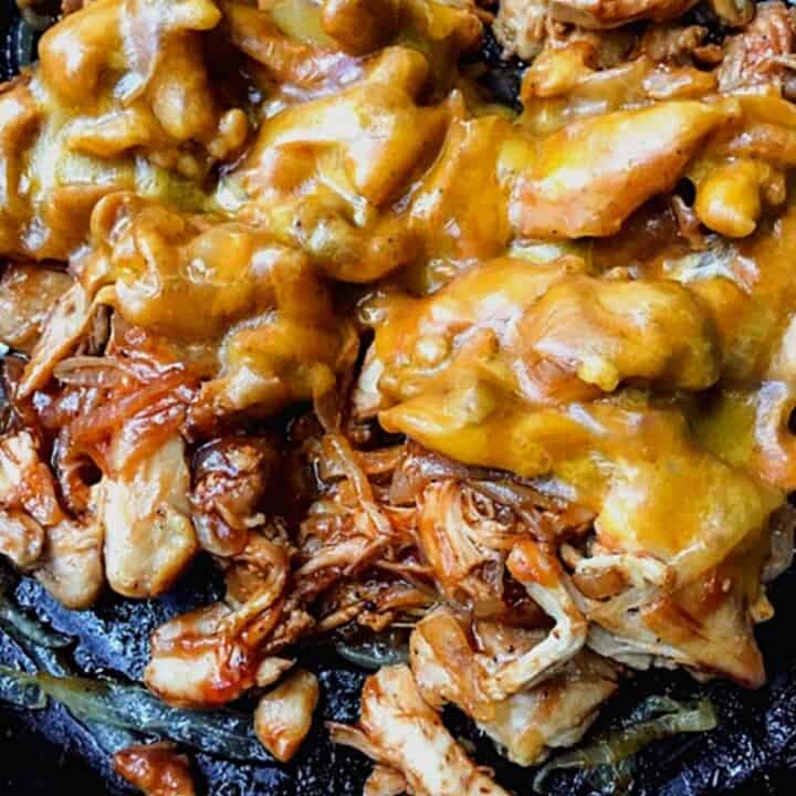 bbq chicken thighs with onions and melted cheese in iron skillet