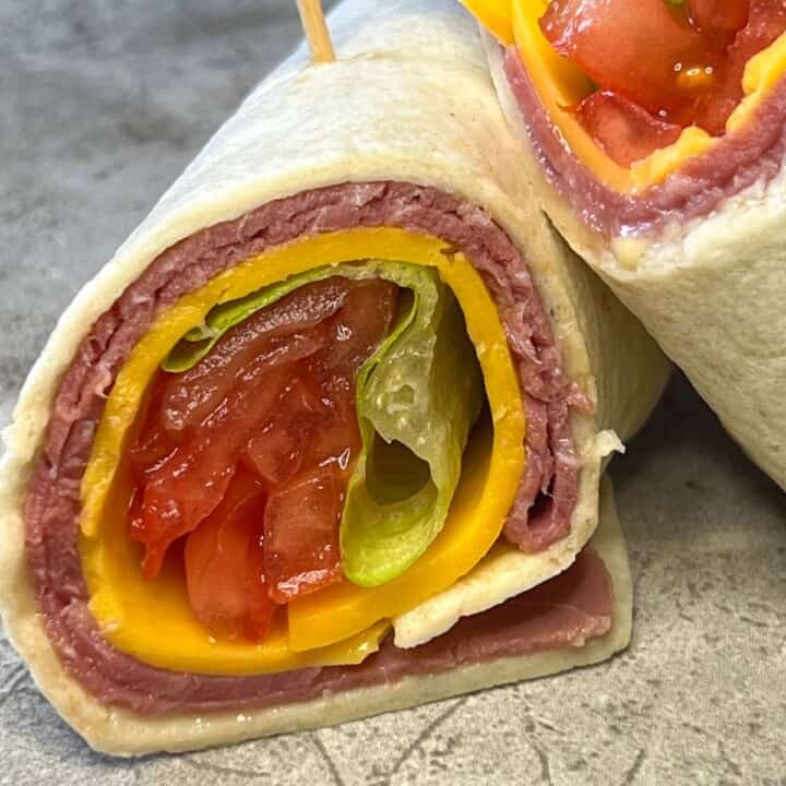 low carb tortilla wrap with roast beef, cheese, lettuce and tomato on marble counter