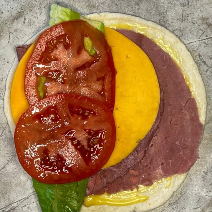 tortilla with layers of roast beef, cheese, lettuce and tomato on marble counter