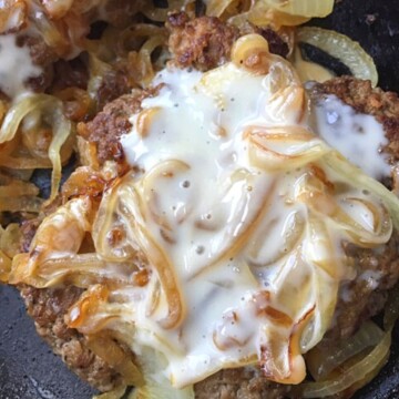burger patty with queso and onions on top in black skillet