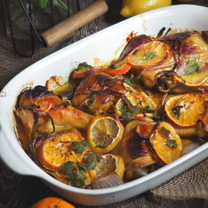 white baking dish with golden brown roasted chicken topped with orange slices