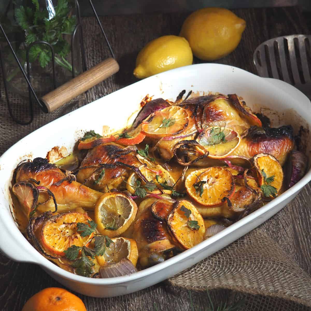 white platter with golden brown roasted chicken and cooked orange slices on top