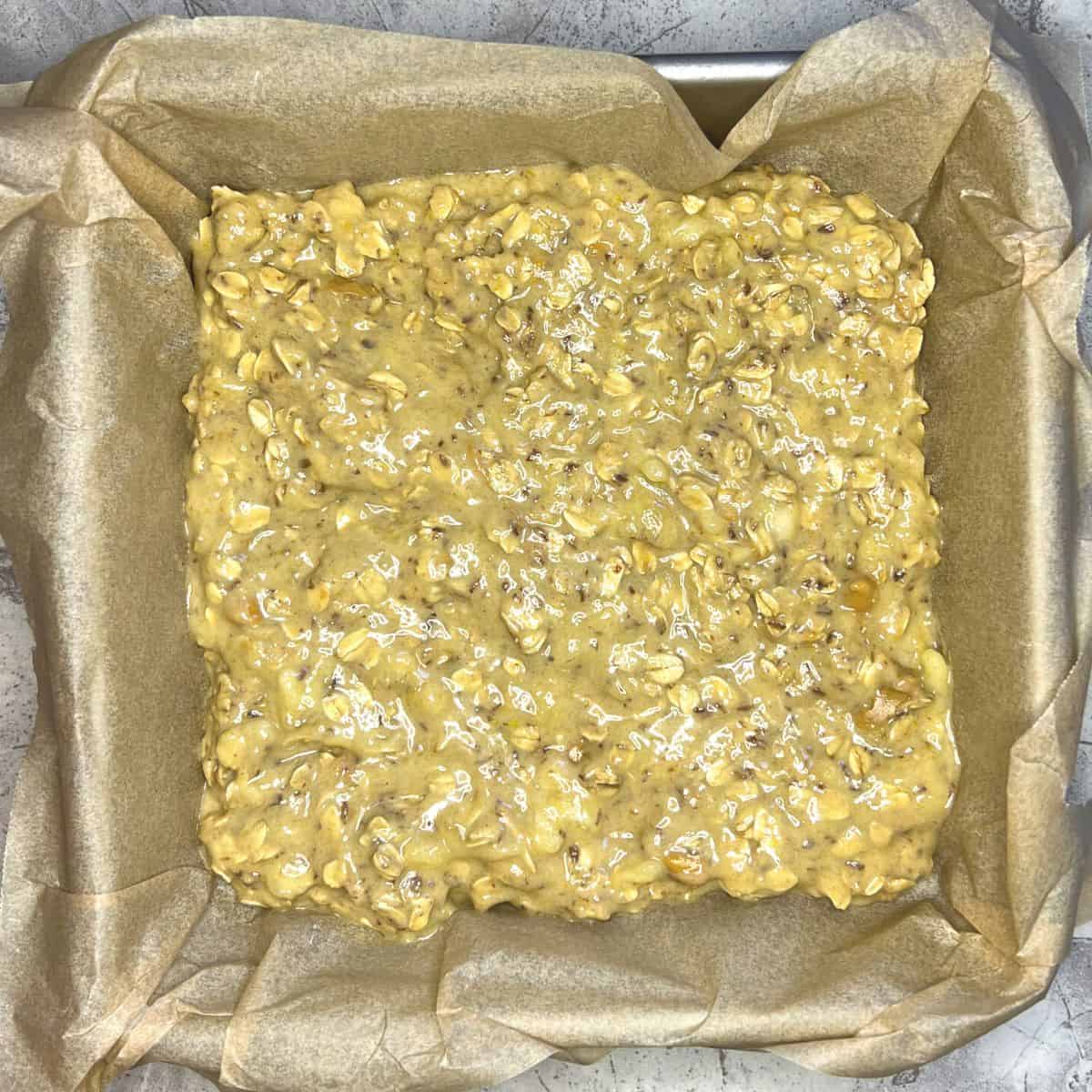 peanut butter banana oat bar batter in parchment lined pan ready for oven