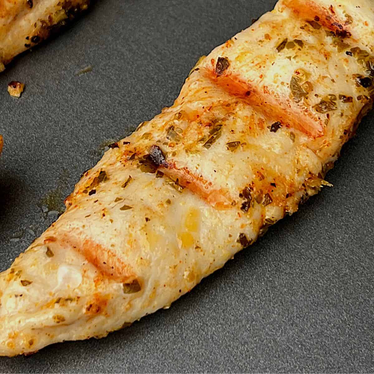 grilled chicken tender with pesto on dark plate
