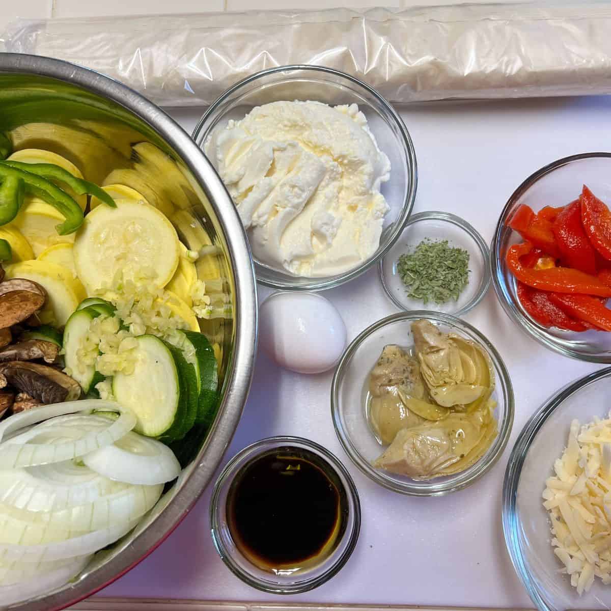 bowls of sliced veggies, cheese,roasted red peppers,seasonings for mediterranean pizza