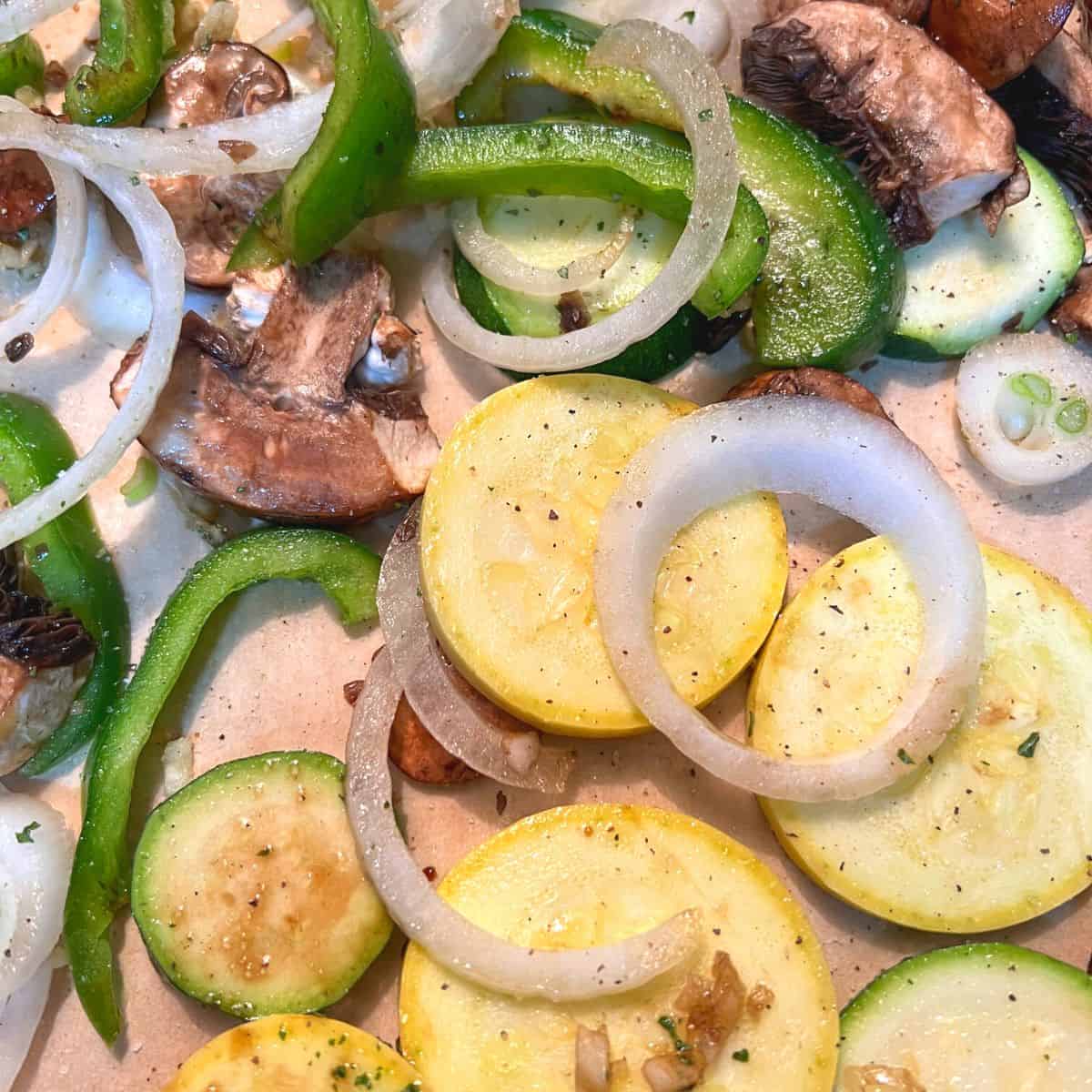 sliced yellow squash, green bell peppers, onions and mushrooms on baking sheet