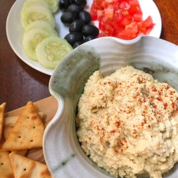 hummus in pottery bowl with sliced cucumbers, olives ,tomatoes and crackers