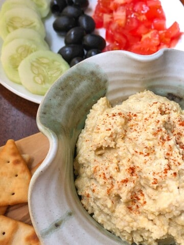 hummus in pottery bowl with sliced cucumbers, olives ,tomatoes and crackers