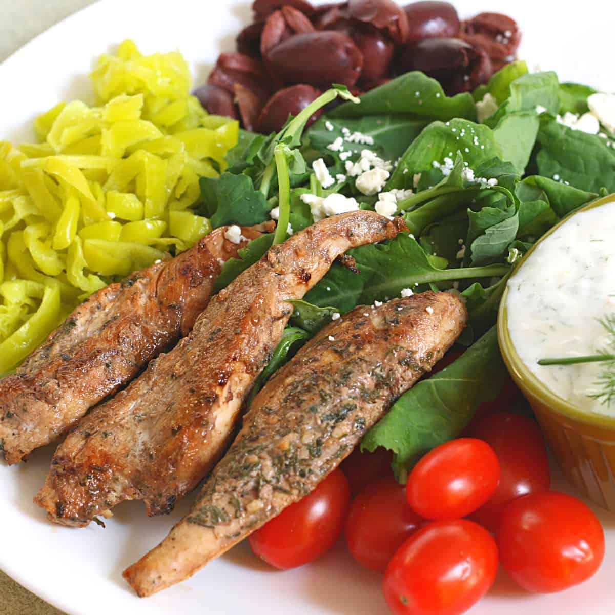 greek chicken tenders, cherry tomatoes, tzatziki sauce, olives on white plate