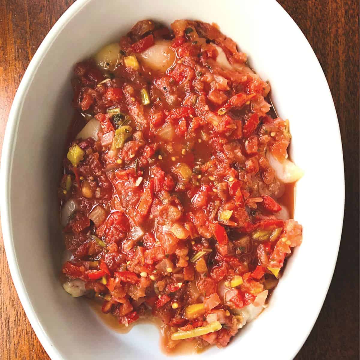 raw chicken tenders covered in salsa in white casserole dish