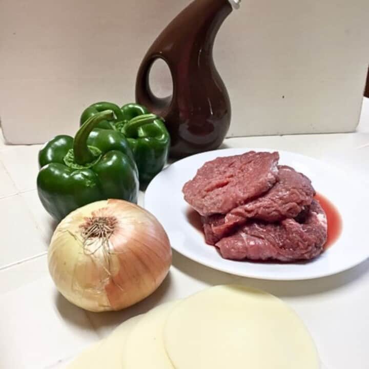 ingredients for stuffed peppers. green peppers, yellow onion, raw beef and olive oil bottle