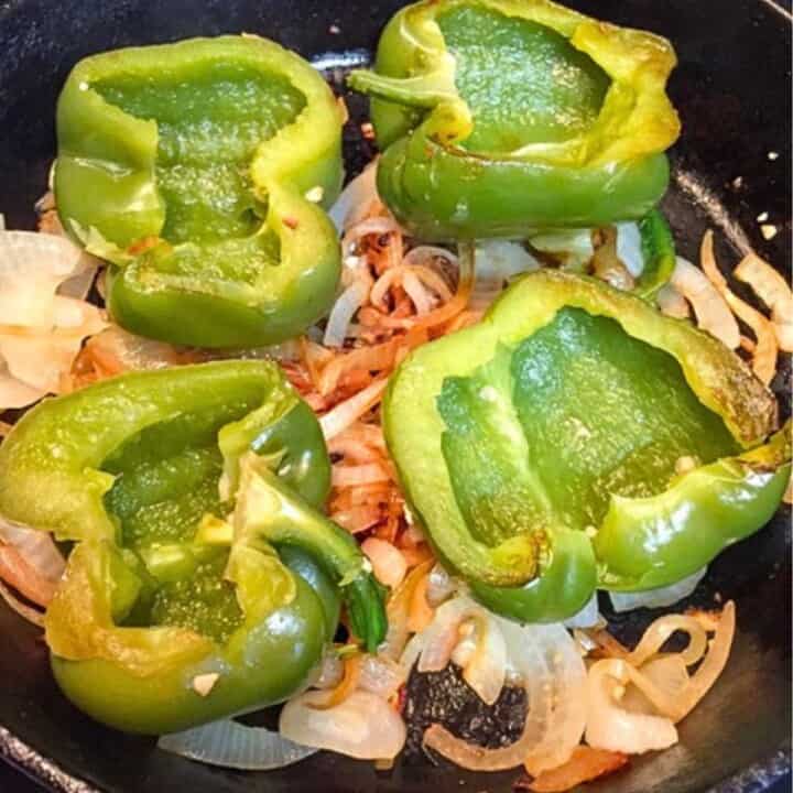 green bell peppers on a bed of sliced onions in black skillet