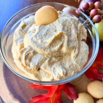 Pumpkin fluff dip in bowl with fall leaves and mini vanilla wafers.
