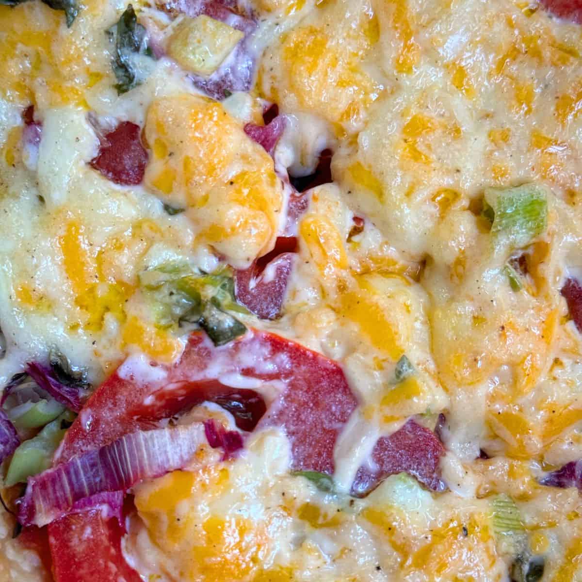Closeup of tomato pie with bits of cheese, tomatoes and green onions.