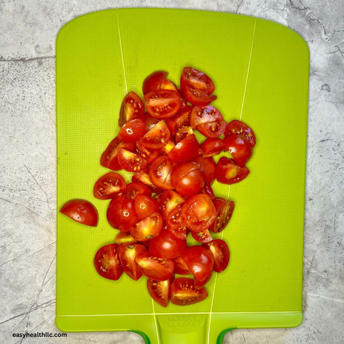 Halved cherry tomatoes on green chopping board.