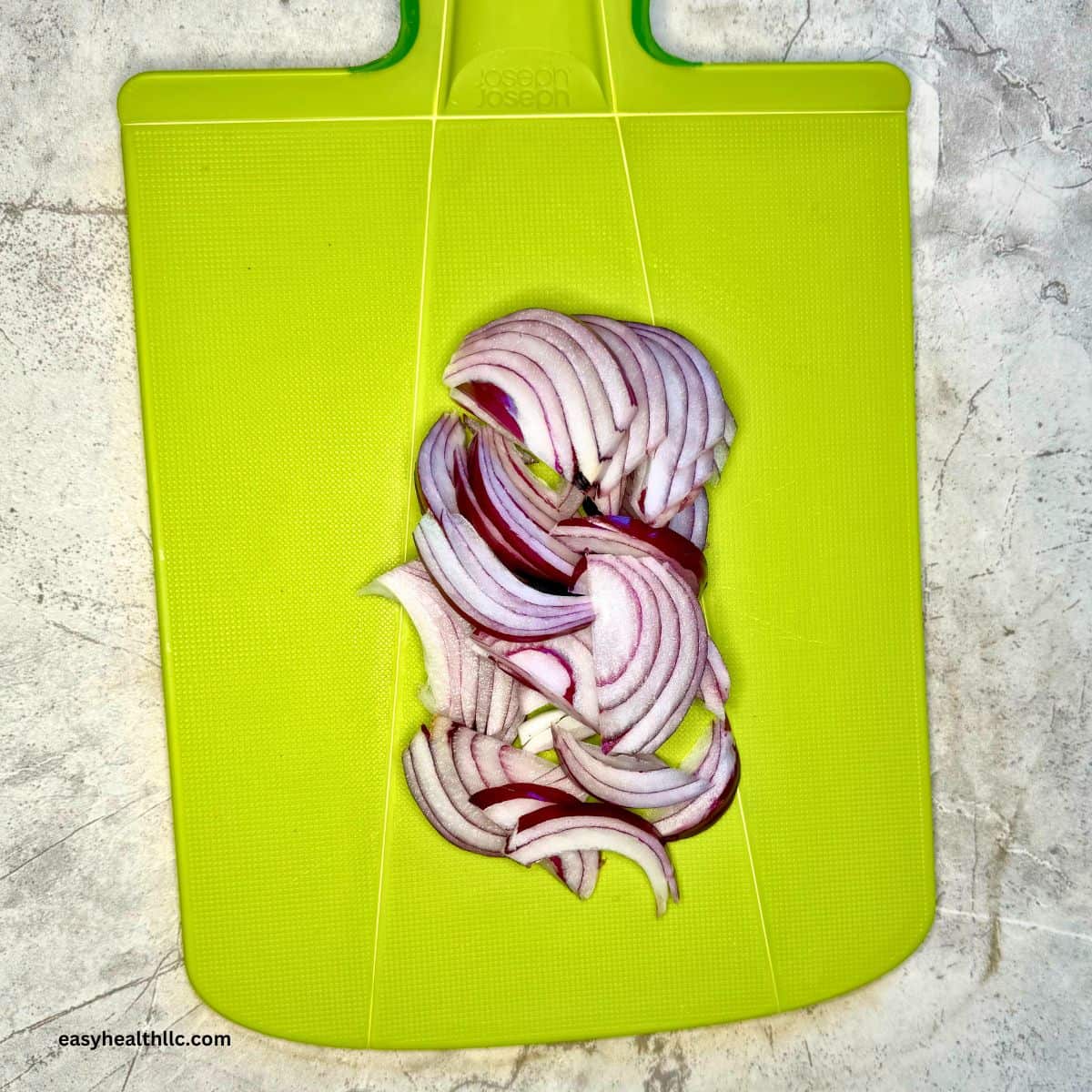 Sliced red onion on green chopping board.