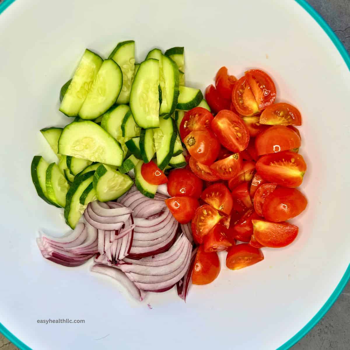 Sliced red onion, cucumber, tomatoes in a bowl.