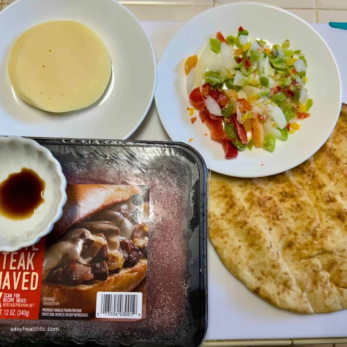 White board with box of shaved steak, peppers and onion, cheese and a pita bread